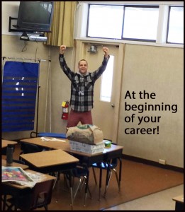 A man standing in front of desks with his arms raised.